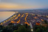 Blick von oben auf die nächtlich beleuchtete Stadt Nizza. Links die Strandpromenade und das Meer.